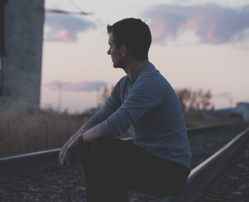 Man sitting on railroad tracks looking at sunset.